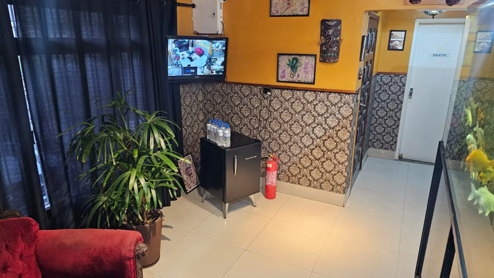 Espera com poltrona de veludo vermelho, planta e TV